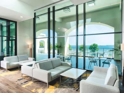 Helles Wohnzimmer mit großen Glasfenstern, modernen grauen Sofas und Blick auf Terrasse und See.