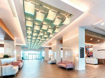 Großer heller Hotellobby mit moderner Deckenbeleuchtung, Sofas rechts und links, und Rezeption im Hintergrund.