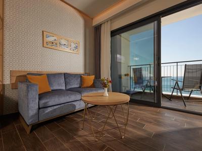 Modernes Wohnzimmer mit grauem Sofa, runden Holztisch und Balkon mit Blick aufs Meer.