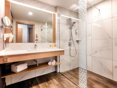 Großer Außenpool mit eingebauten Liegen, umgeben von Terrasse und mit Blick auf Bäume und See.