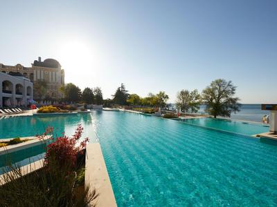 Gran piscina con agua clara junto a edificios del hotel bajo un cielo soleado.