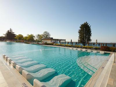 Piscina exterior con tumbonas dentro del agua y vista al lago bajo cielo despejado.
