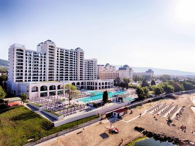 Frau macht Yoga in weißer Kleidung, steht auf einem Bein im Wald mit hohen Bäumen und grünem Gras.