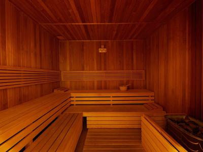 Innenraum einer Sauna mit hellen Holzbänken und Wänden aus dunklem Holz, warme Beleuchtung.