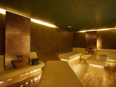 Hell beleuchteter, moderner Wellness-Spa-Raum mit braunen Fliesen, Sitzbänken und entspannter Atmosphäre.