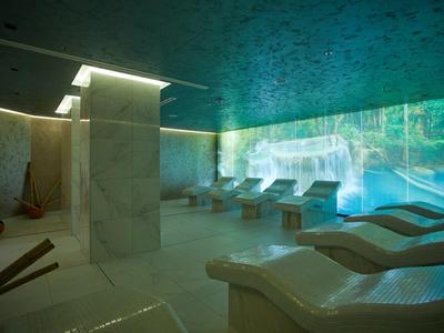 Moderner Wellnessraum mit Marmorwänden, Liegen und projizierten Naturbildern an einer Wand.