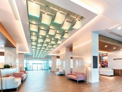 Vestíbulo de hotel moderno y luminoso con bancos e iluminación de techo estructurada.