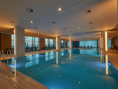 Moderner Innenpool mit großen Fenstern, sanfter Beleuchtung und klar reflektierendem Wasser.