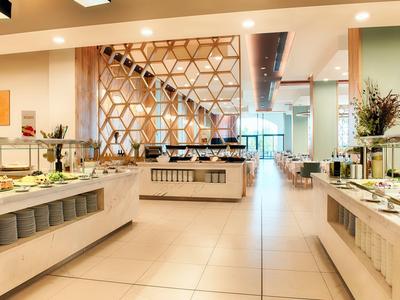 Modernes Buffet mit weißen Theken, Glasschutzelementen und vielfältigen Speisen in hellem Raum.