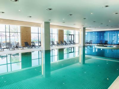 Moderner Innenpool mit großen Fenstern, ruhigem Wasser und Liegestühlen entlang der Seiten.