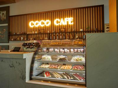 Modernes Café mit beleuchtetem Schriftzug, Kuchen- und Gebäckvitrine, warmes Holz- und Marmordesign.