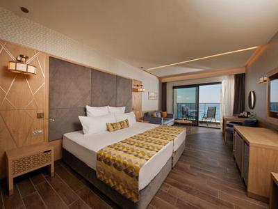 Modern eingerichtetes Hotelzimmer mit großem Bett, Holzboden und Blick auf Meer durch Panoramaglaswand.