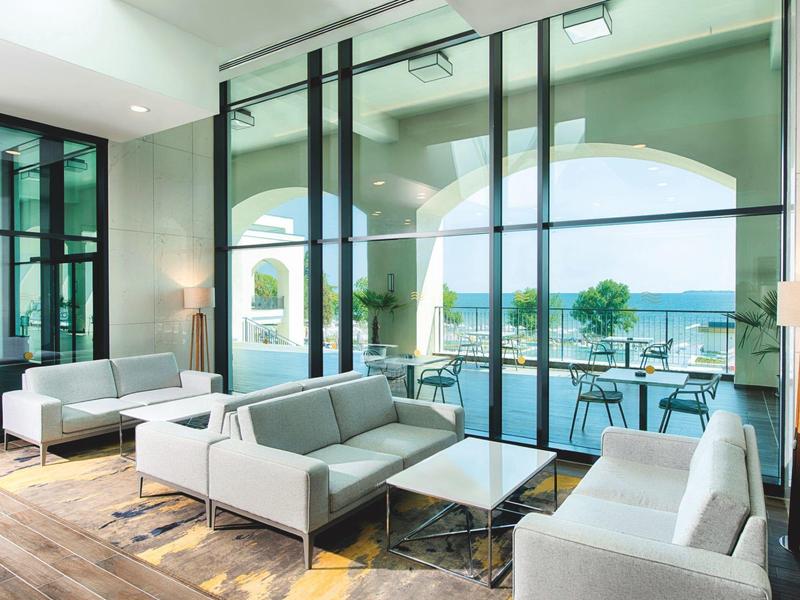 Helles Wohnzimmer mit großen Glasfenstern, modernen grauen Sofas und Blick auf Terrasse und See.