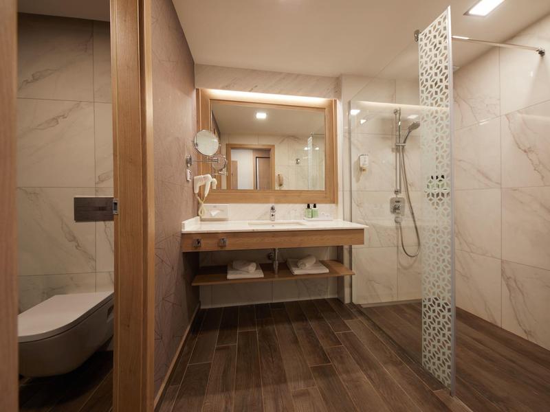 Modernes Badezimmer mit Holzdekor, Glas-Dusche, großem Spiegel und wandmontiertem WC.