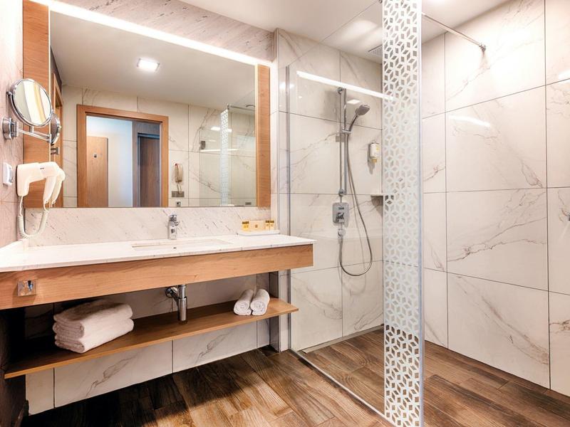 Großer Außenpool mit eingebauten Liegen, umgeben von Terrasse und mit Blick auf Bäume und See.