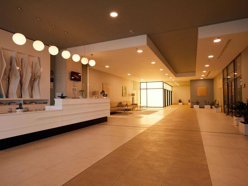 Großer, moderner Empfangsbereich mit hellem Boden, Theke, runden Deckenlampen und Sitzgelegenheiten.