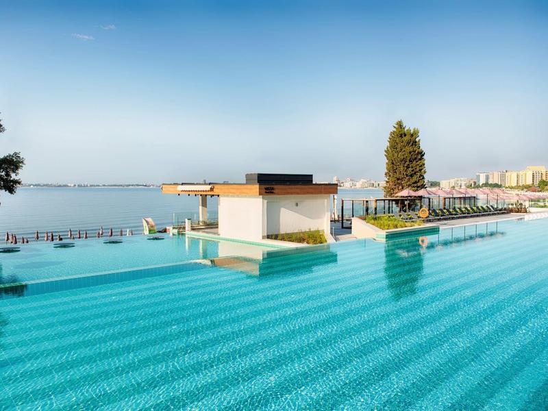 Großer Infinity-Pool mit türkisfarbenem Wasser und Blick auf das blaue Meer und entfernte Stadt.