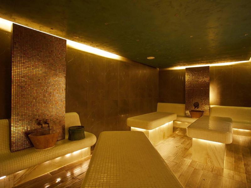 Hell beleuchteter, moderner Wellness-Spa-Raum mit braunen Fliesen, Sitzbänken und entspannter Atmosphäre.