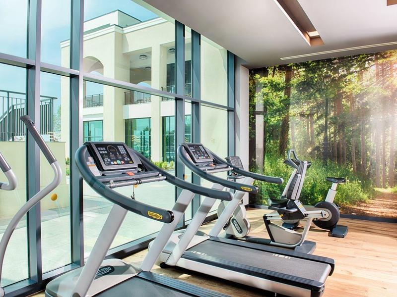 Moderner Fitnessraum mit Laufbändern, Fahrrädern und großem Fenster mit Gartenblick.