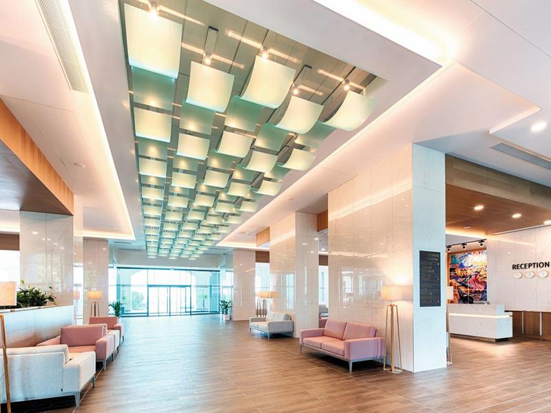 Großer, heller Lobbybereich mit moderner Deckenleuchte, weißen Säulen und rosa Sitzbänken.