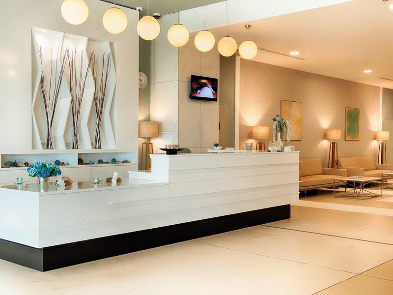 Heller Empfangsbereich mit modernem weißen Tresen, runden Deckenlampen und gemütlichen Sitzplätzen.
