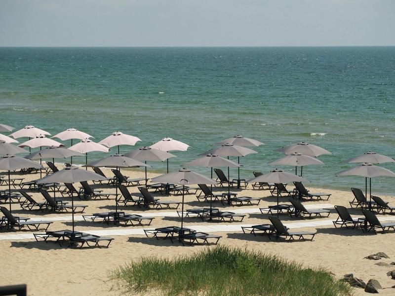 Sandstrand mit vielen Liegen und weißen Sonnenschirmen vor ruhigem, blau-grünem Meer.