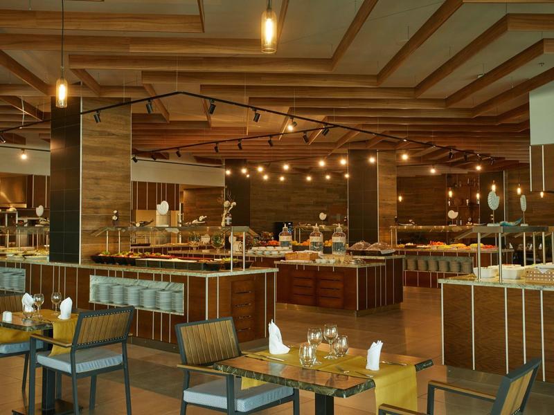 Großes, warm beleuchtetes Restaurant mit Holzdecke, Tischen, Stühlen und Buffetbereich.