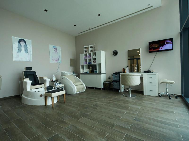 Moderner Friseursalon mit Stuhl, Waschbecken, Spiegel, weißen Möbeln und großen Fenstern.