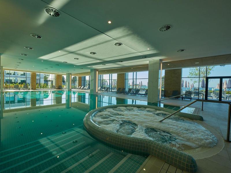 Moderner Indoor-Pool mit großem Whirlpool, bodentiefen Fenstern und natürlichem Tageslicht.