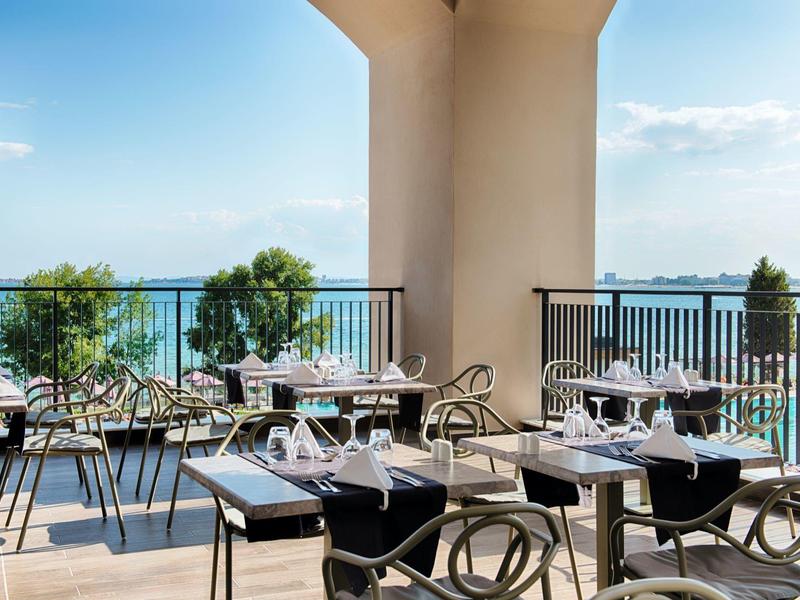 Terrassenrestaurant mit Tischen, Stühlen, Weingläsern und Blick auf das Meer und blauen Himmel.