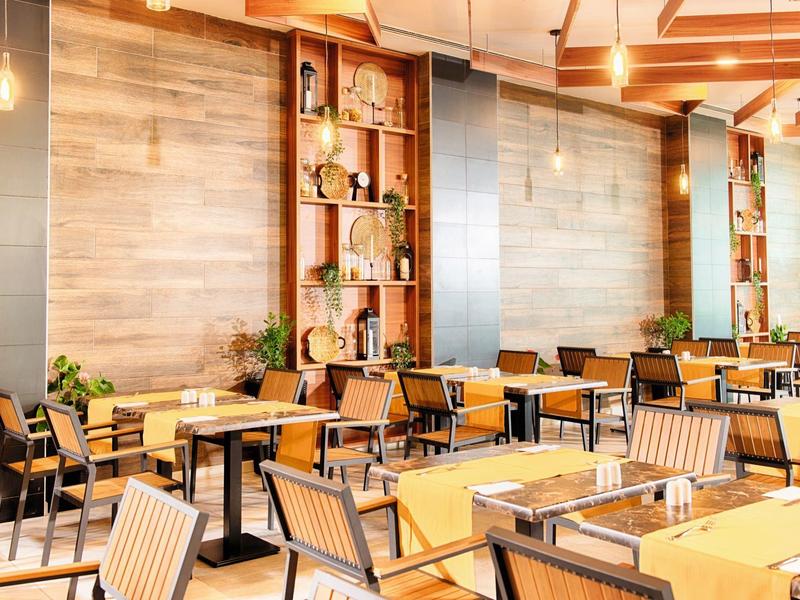 Helles Restaurant mit Holzvertäfelungen, Pflanzen und modernen Stühlen an rechteckigen Tischen.