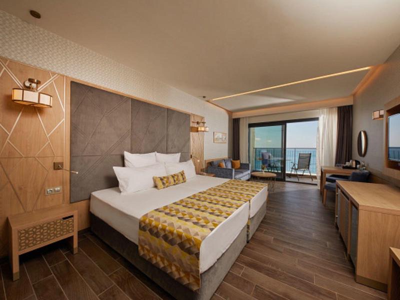 Modern eingerichtetes Hotelzimmer mit großem Bett, Holzboden und Blick auf Meer durch Panoramaglaswand.