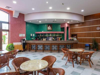 Cozy hotel bar area with brown chairs, marble tables, and green bar wall.