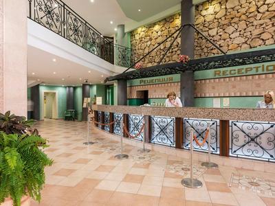 Bright hotel lobby with reception and seating area, decorated with plants and wood details.