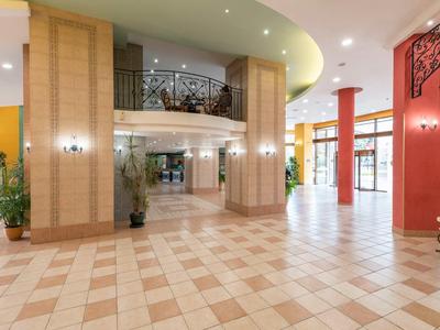 Spacious hotel lobby with marble floor, decorative columns, and balcony on the first floor.