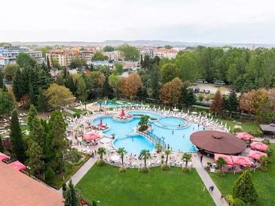 Large hotel pool with umbrellas and lounge chairs, surrounded by trees and cityscape in the background