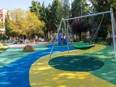 Colorful playground with swings and climbing structures in a tree-surrounded park.