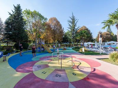 Colorful children's playground with carousel and slide in hotel garden on a sunny day.