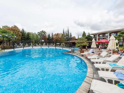 Large hotel pool with sun loungers and umbrellas under a cloudy sky.