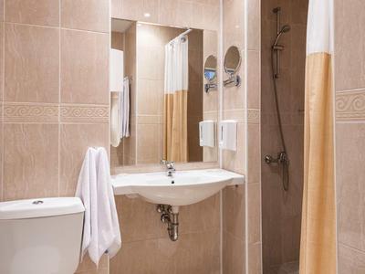 Modern bathroom with sink, toilet, and shower with curtain in warm beige tones.