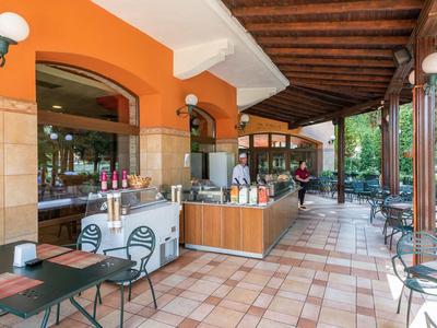Covered restaurant terrace with tables, chairs, and service counter in orange and wood tones.