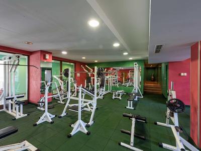 Gimnasio moderno con varios equipos de ejercicio y suelo alfombrado verde.