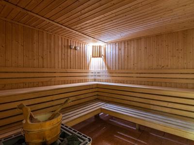Sauna interior con paneles de madera, bancos y cubo de sauna con cucharón