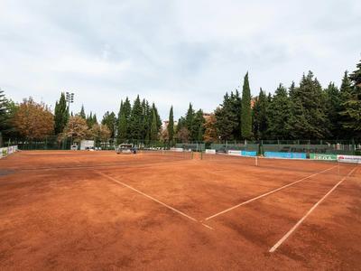 Pista de tenis de tierra batida vacía rodeada de árboles bajo cielo nublado