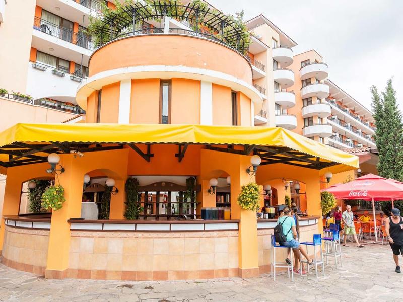 Round orange café with yellow awning in front of a hotel building with balconies.