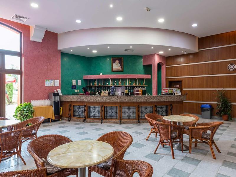 Cozy hotel bar area with brown chairs, marble tables, and green bar wall.
