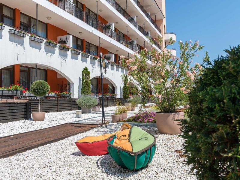 Hotel outdoor area with white gravel, plants, and colorful cushions near balconies.