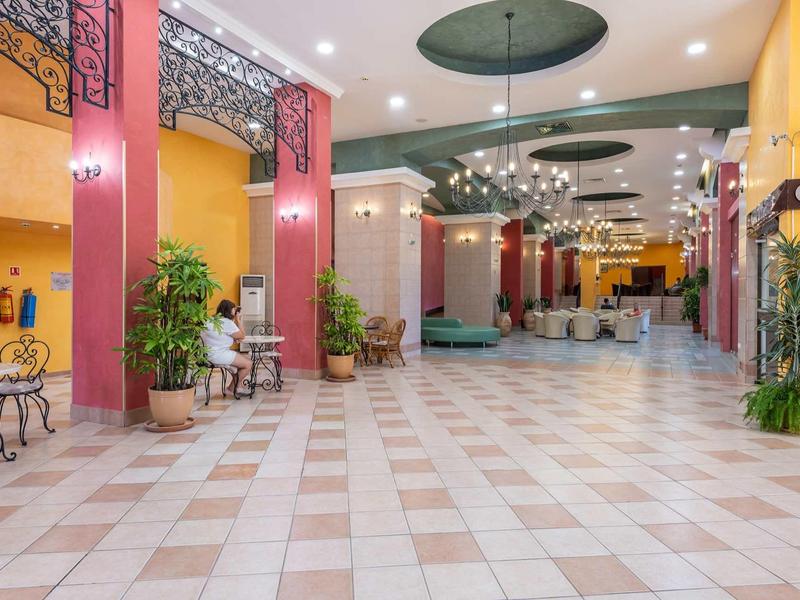 Spacious, bright hotel lobby with red columns, seating areas, and plants.