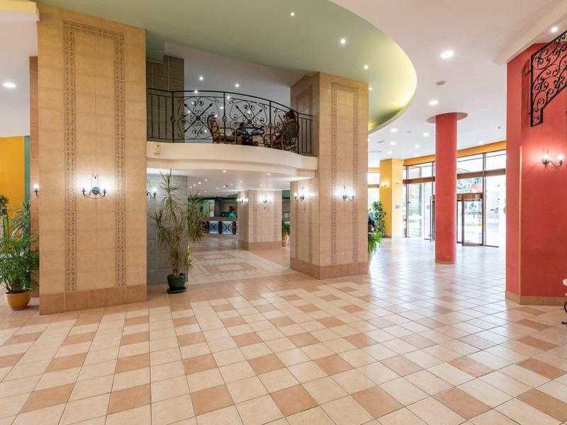 Spacious hotel lobby with marble floor, decorative columns, and balcony on the first floor.