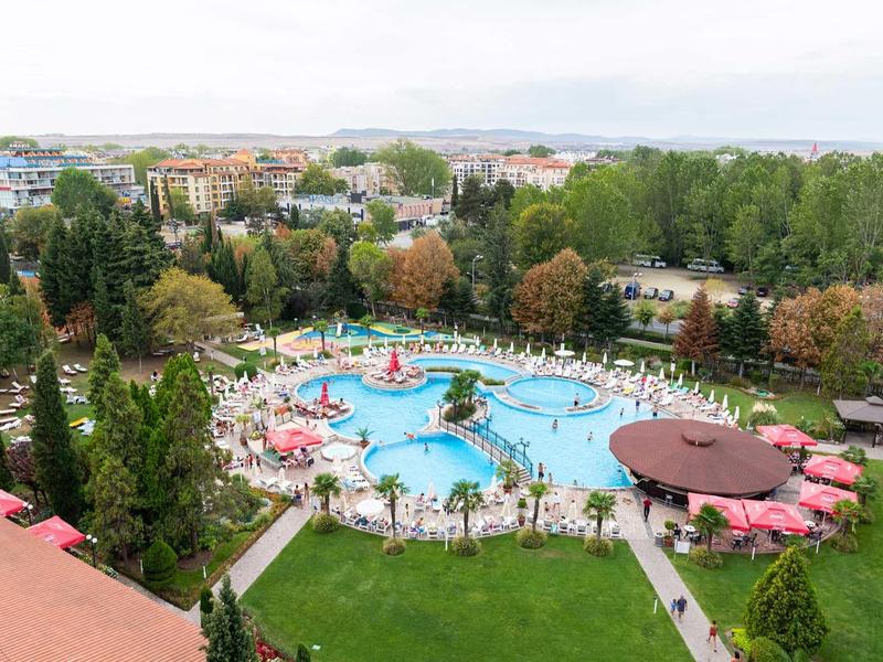 Large hotel pool with umbrellas and lounge chairs, surrounded by trees and cityscape in the background